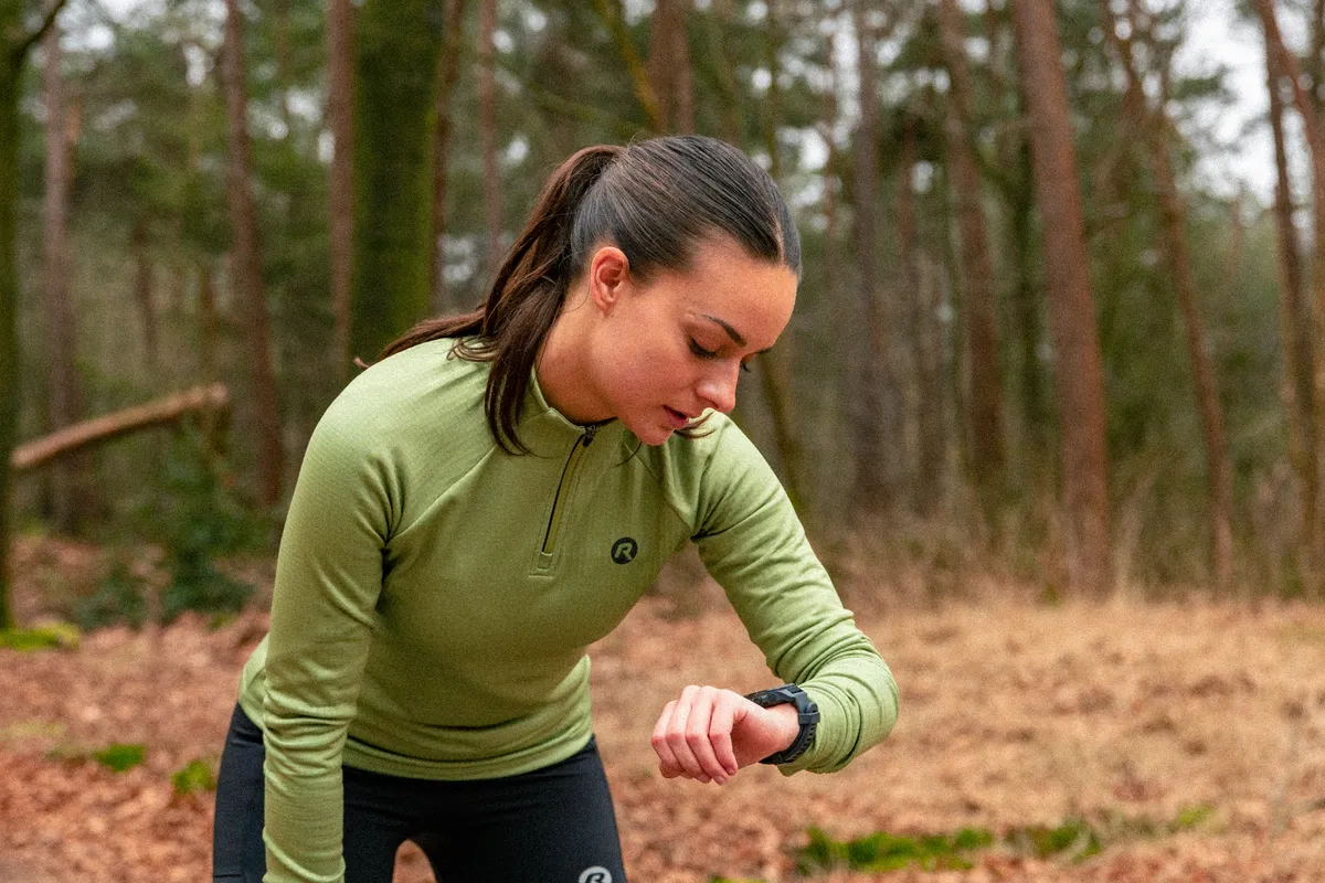 Wielrenster in Rogelli-kleding kijkt op haar sporthorloge tijdens een training in het bos