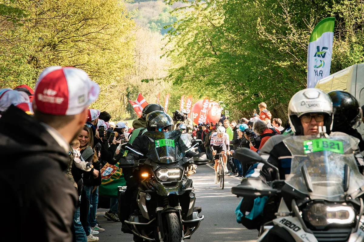 Toeschouwer volgt het wielerparcours vanaf een klapstoel bij een oude schuur