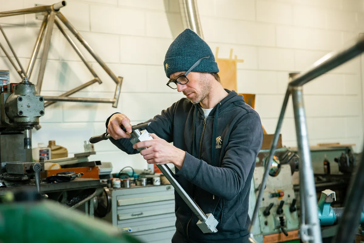 Framebouwer van St. Joris Cycles bewerkt een stalen buis aan de werkbank