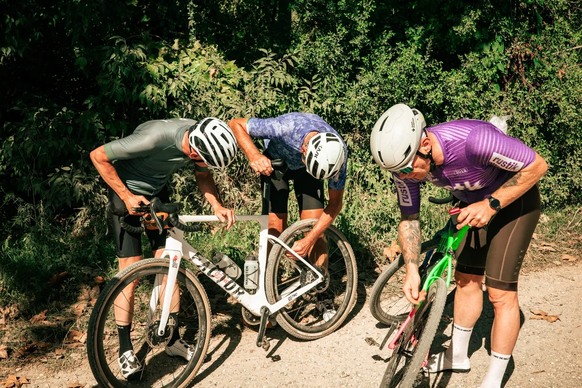 Renners buigen zich over een fiets langs een gravelpad