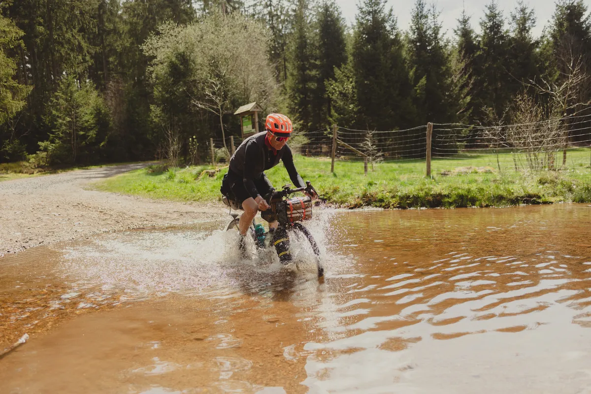 Bikepacker rijdt door een ondergelopen pad, het water spat op