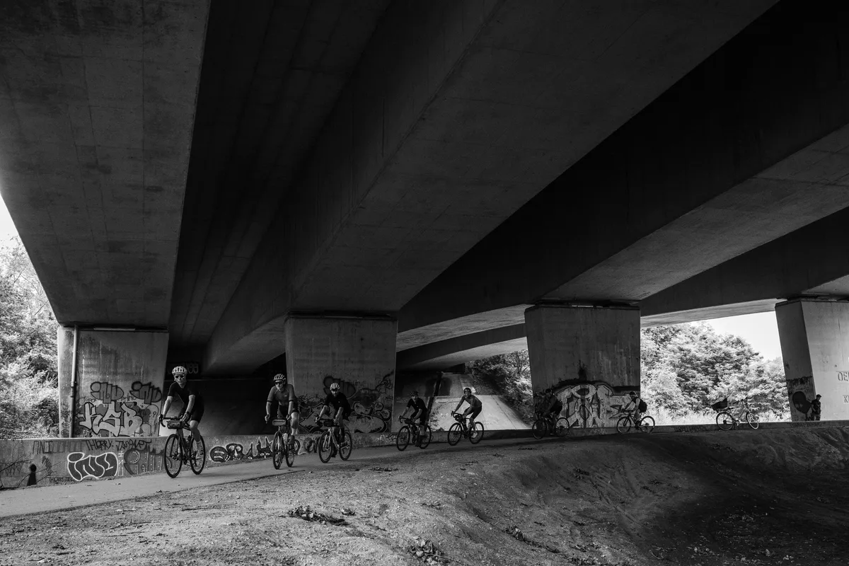 Deelnemers rijden onder een viaduct door, zwart-wit
