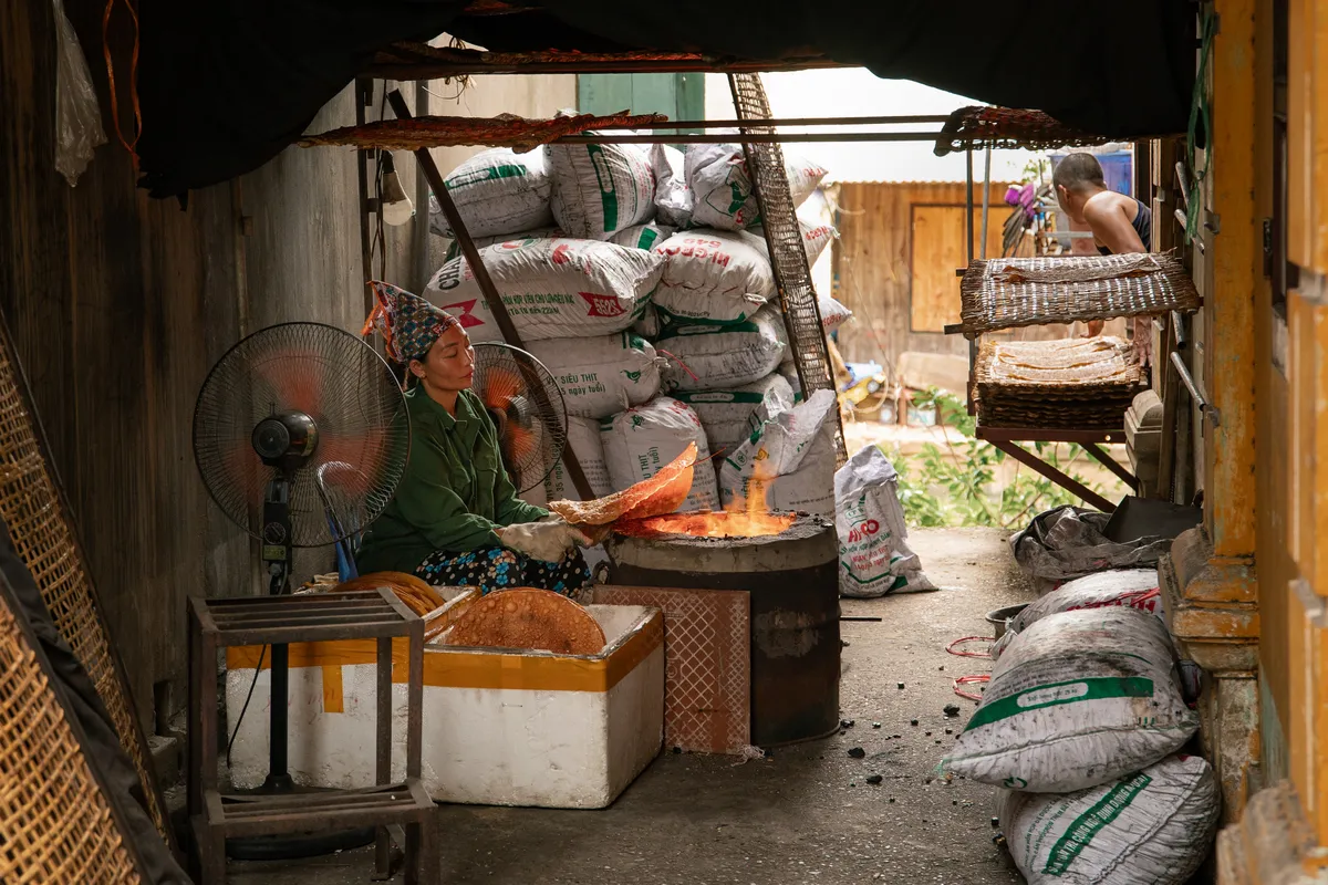 Vrouw bakt rijstpapier boven een houtvuur, Vietnam