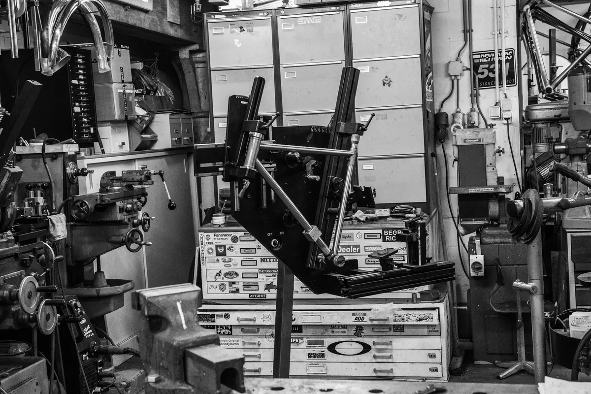 Framebouwer in een werkplaats vol gereedschap, zwart-wit