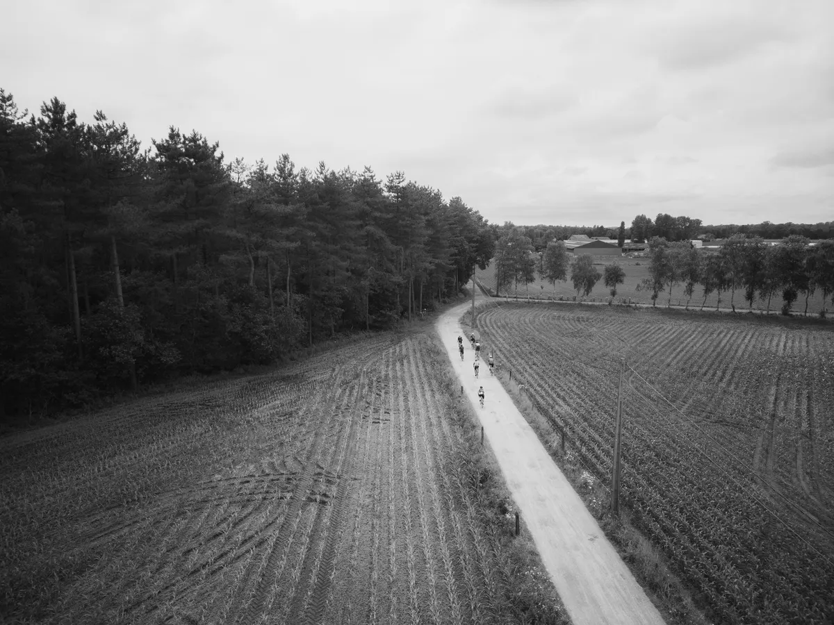 Groep deelnemers op een landweg door de velden, luchtfoto in zwart-wit