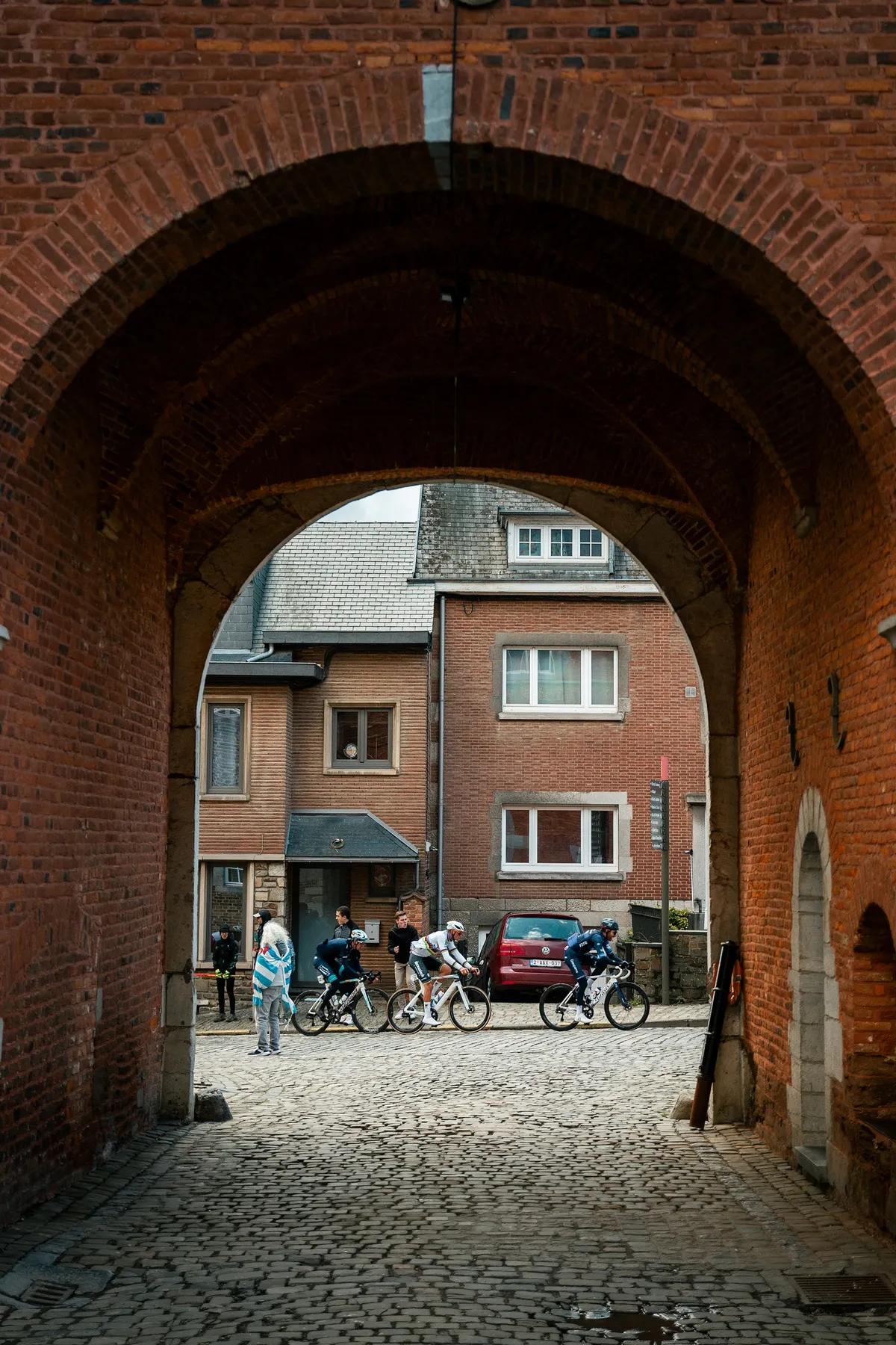 Renners rijden door een bakstenen poort in een dorpskern