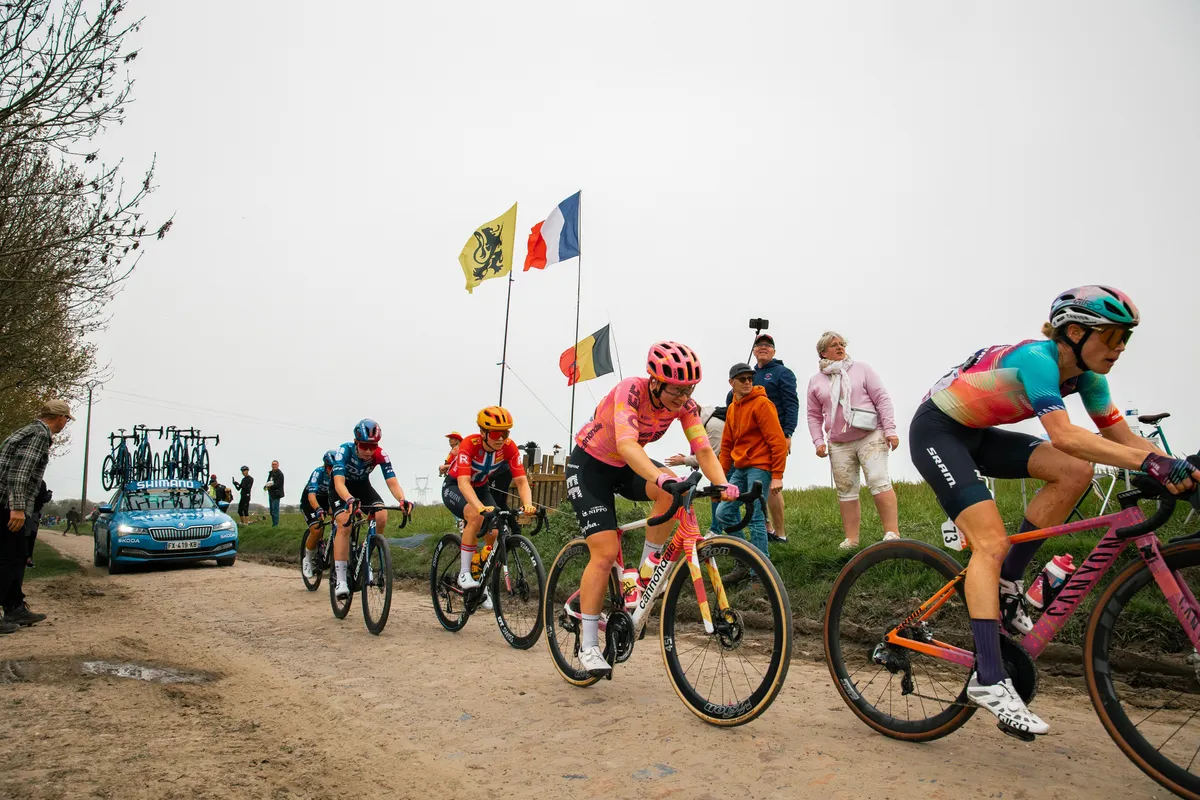 Peloton over de kasseien van Parijs-Roubaix Femmes met vlaggen langs de kant