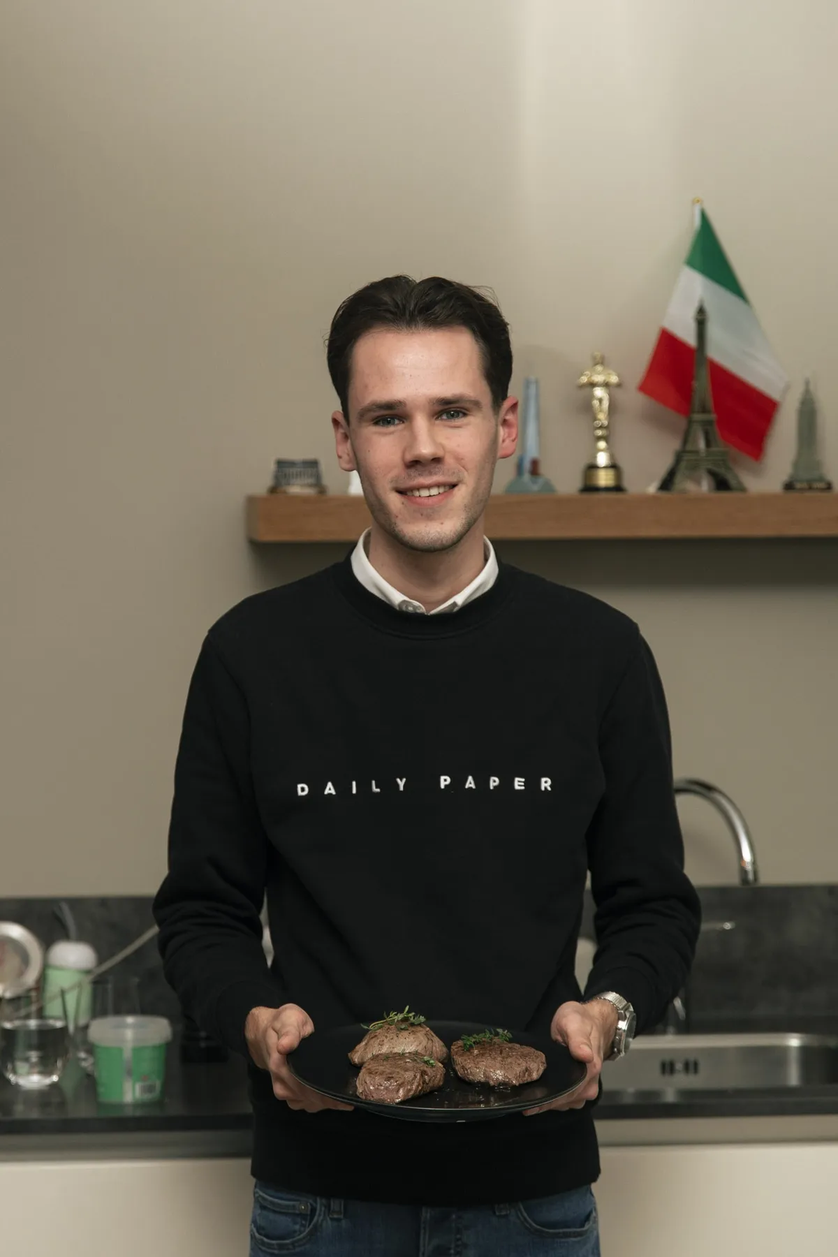 Portret van Jonathan de Koeijer in zijn keuken, met een bord in handen