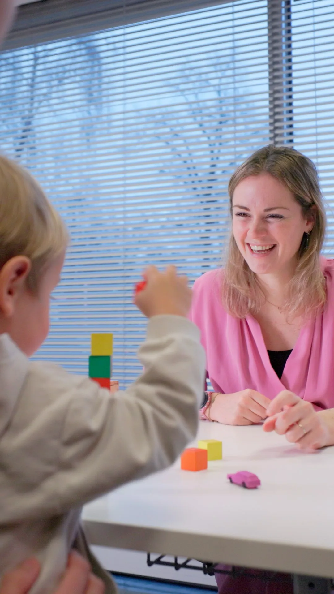Lachende jeugdarts speelt met blokjes tijdens een consult met een jong kind, still uit de campagnevideo voor GGD West-Brabant